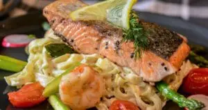 Grilled salmon with crispy skin, served over creamy shrimp pasta with asparagus and cherry tomatoes. A delicious seafood dish from our salmon and shrimp recipes.
